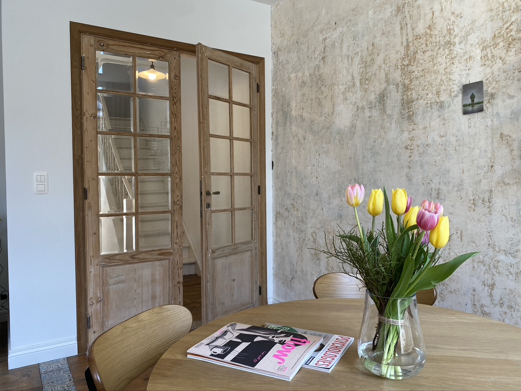 Eettafel met verse tulpen, ruwe kalkwand en openstaande deuren naar de trap